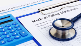 Close-up of a blue calculator and stethoscope sitting on top of a clipboard with a Medical Billing Statement.