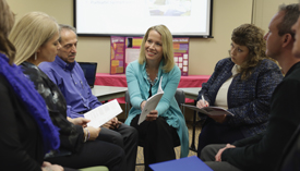 A group of five people sit in a circle in discussion.